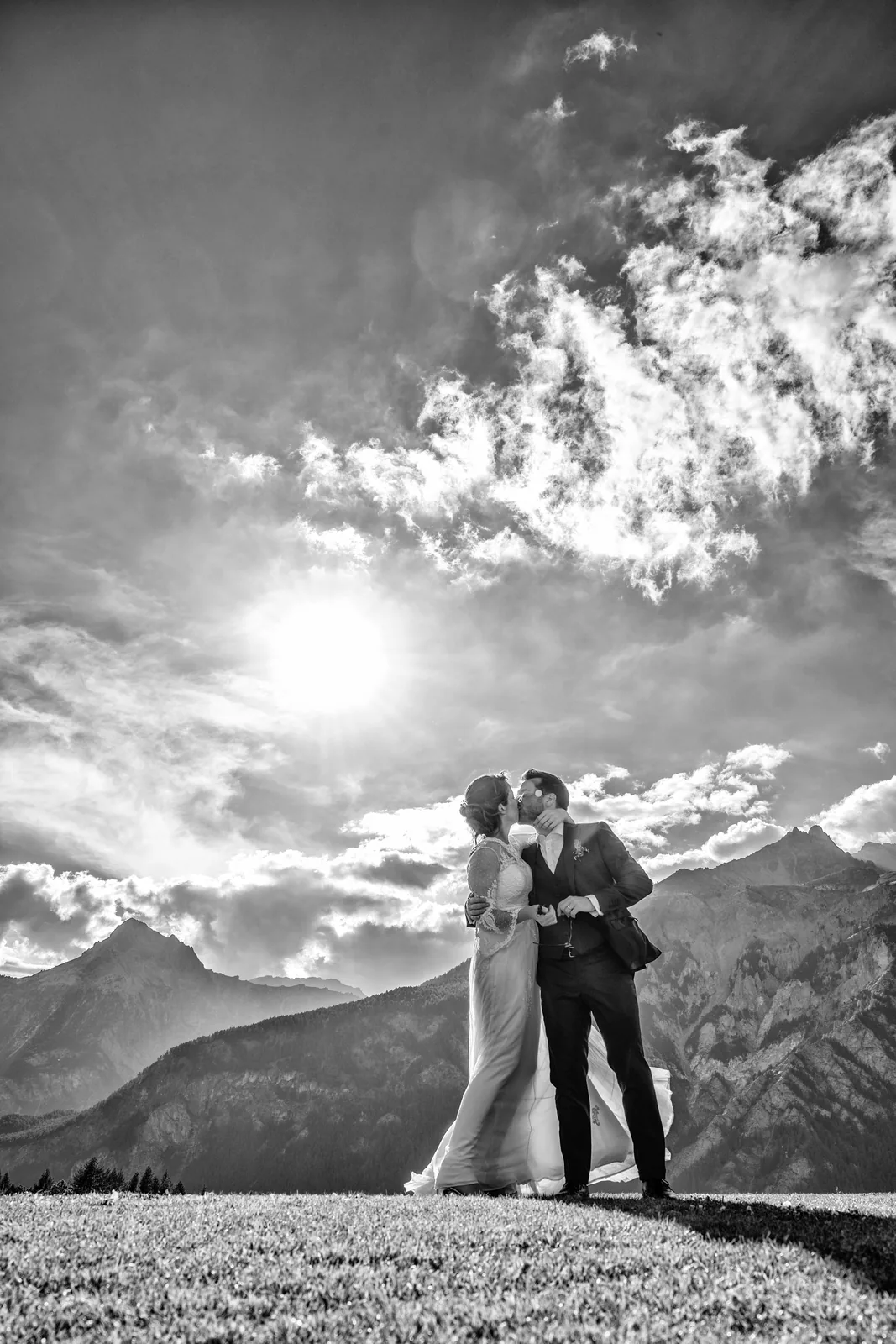 The couple kissing against the sun and clouds above the Alps, black and white
