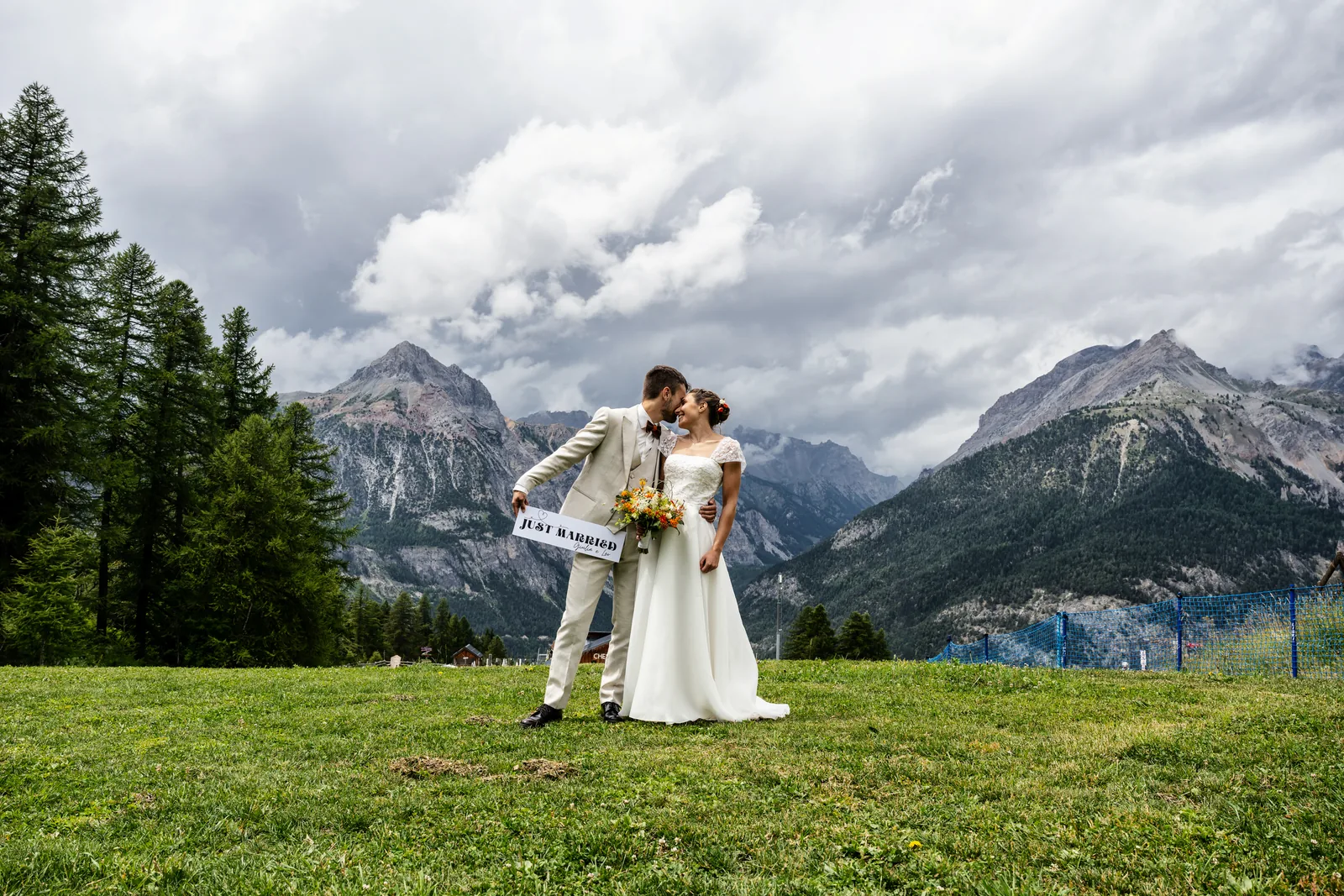 The couple kissing on a mountain meadow beneath dramatic peaks and clouds, Bardonecchia