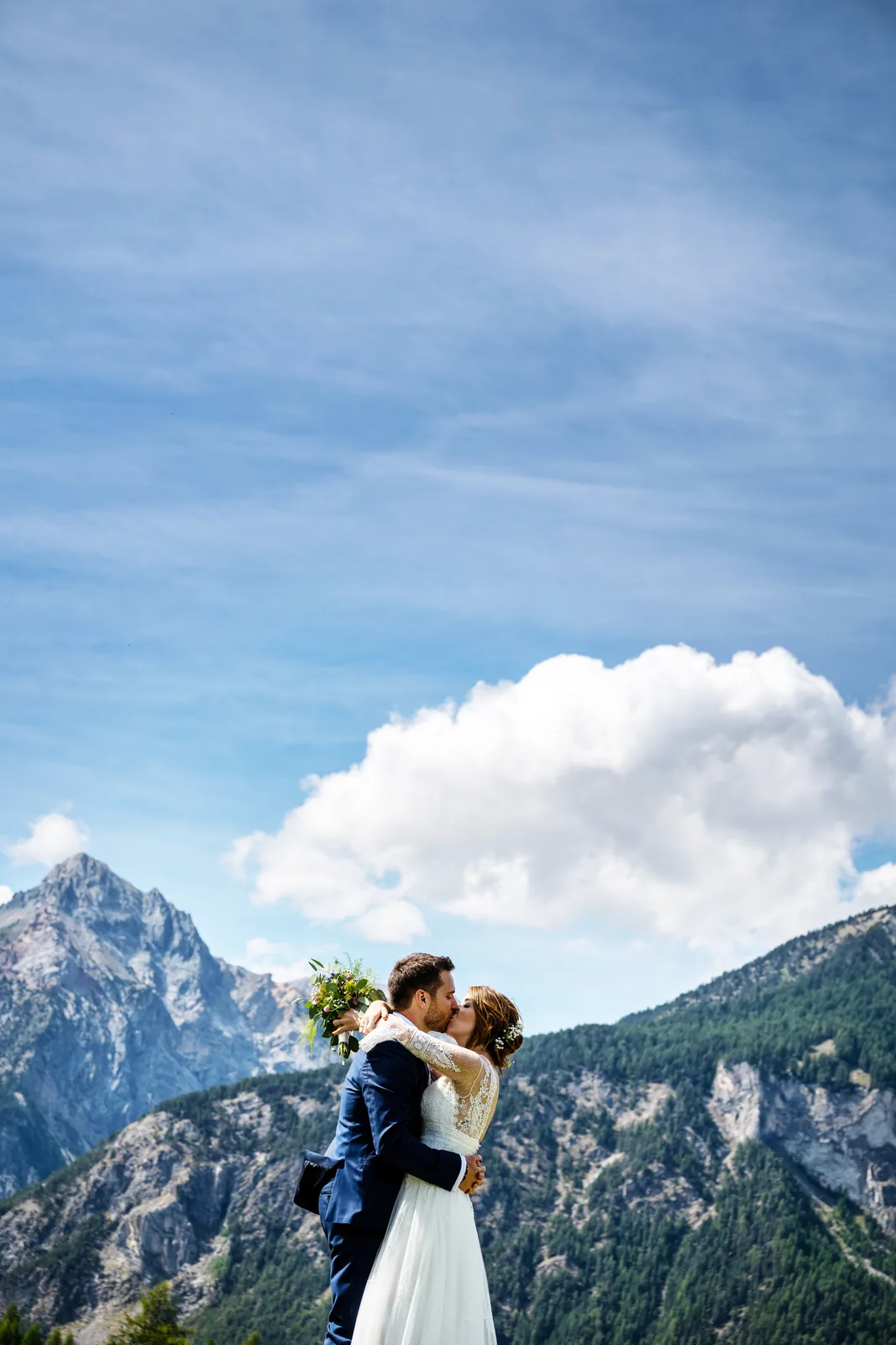 The couple kissing beneath a mountain peak and a white cloud