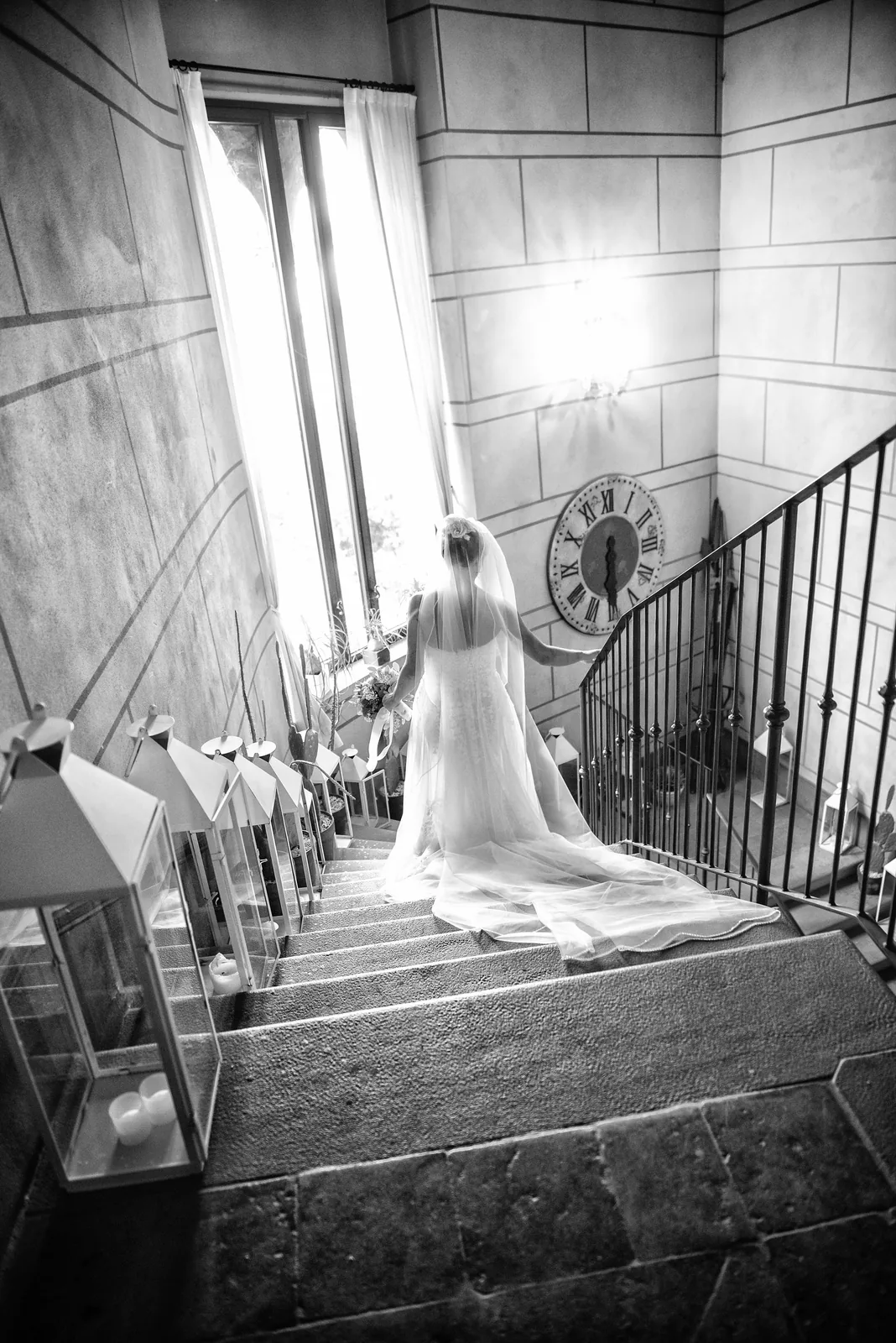 A bride walking down a stone staircase in window light, Castello di Marne, black and white