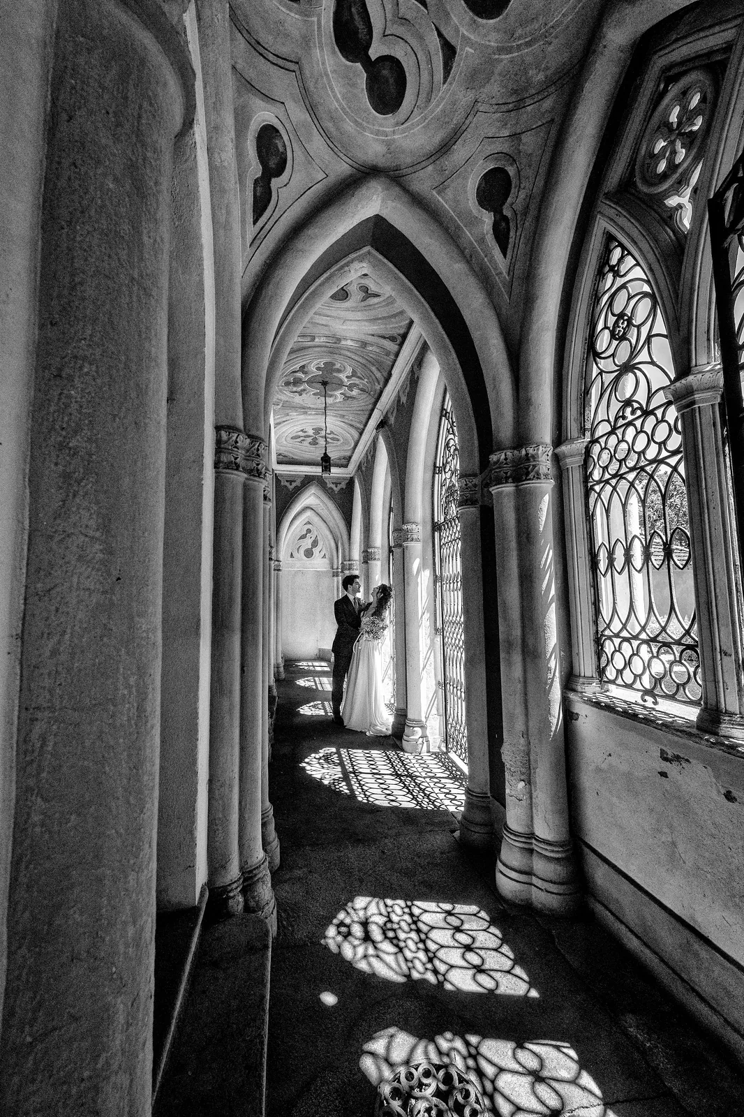 A neo-gothic portico with lace shadows on the floor and the couple at the end, black and white
