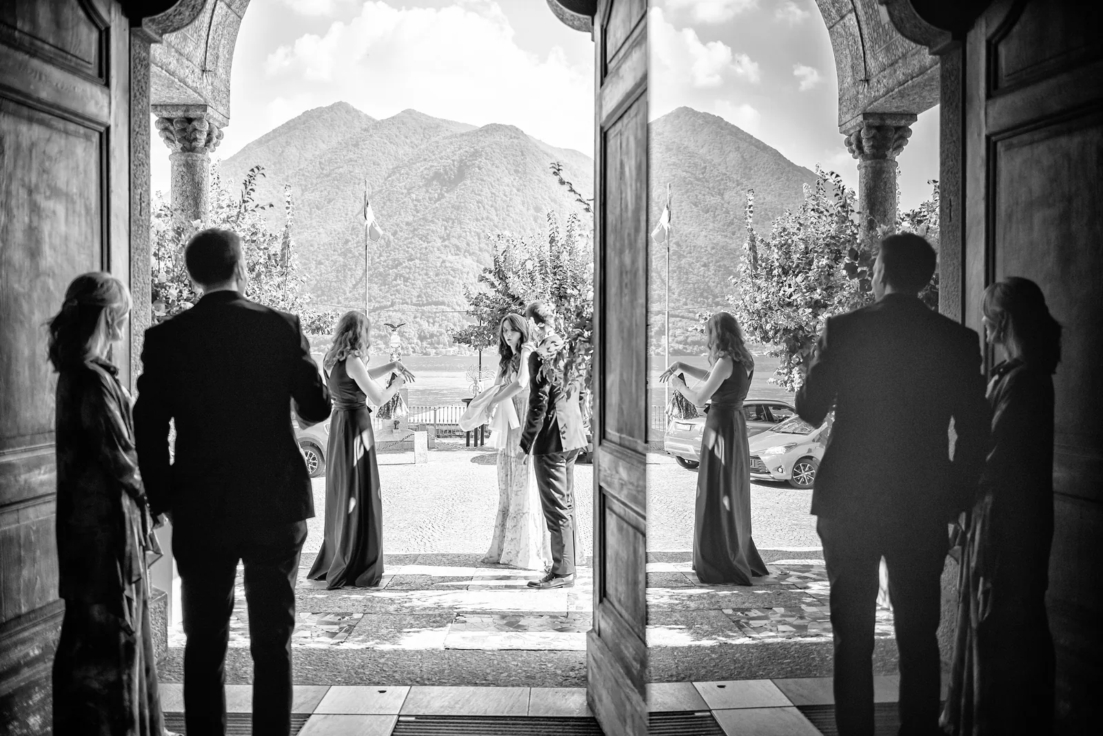 Church doors opening onto Lake Como and its mountains, the couple outside, black and white
