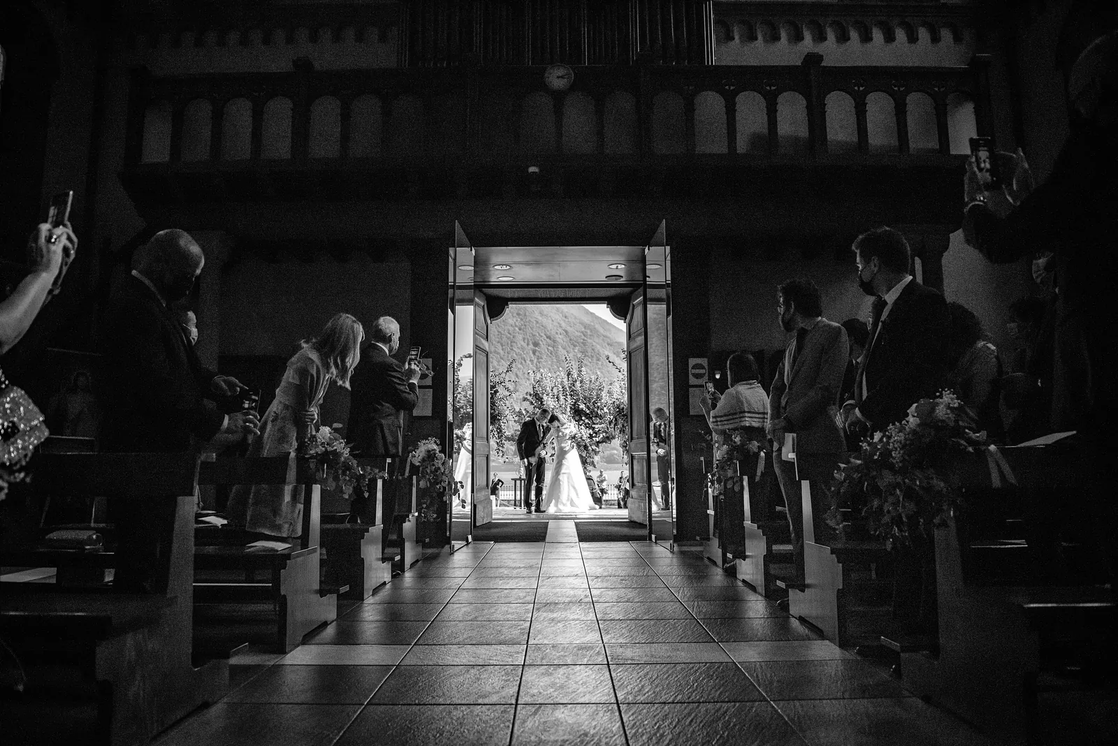 A dark church aisle with the couple in the light of the doorway, Lake Como, black and white