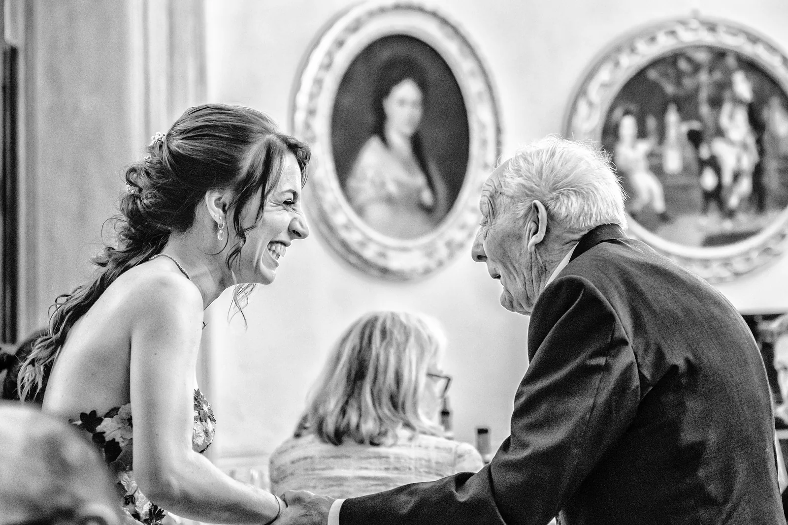 The bride laughing with an elderly guest beneath oval portraits, Palazzo La Marmora, black and white