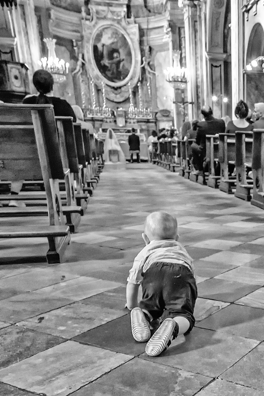 A small child crawling down a baroque church aisle during the ceremony, Turin, black and white