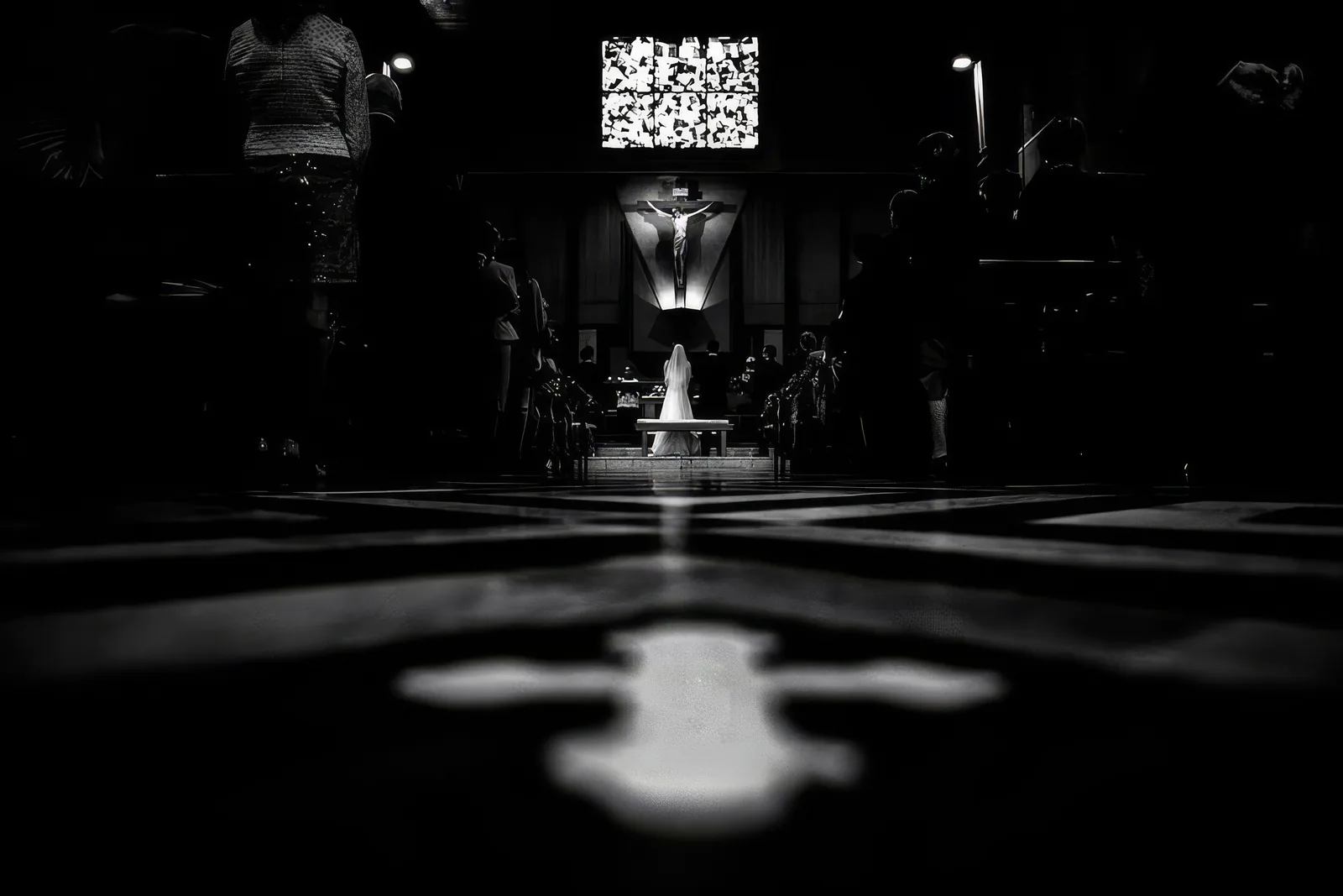 A bride kneeling at the altar in a dark church, a cross of light on the floor, Turin, black and white
