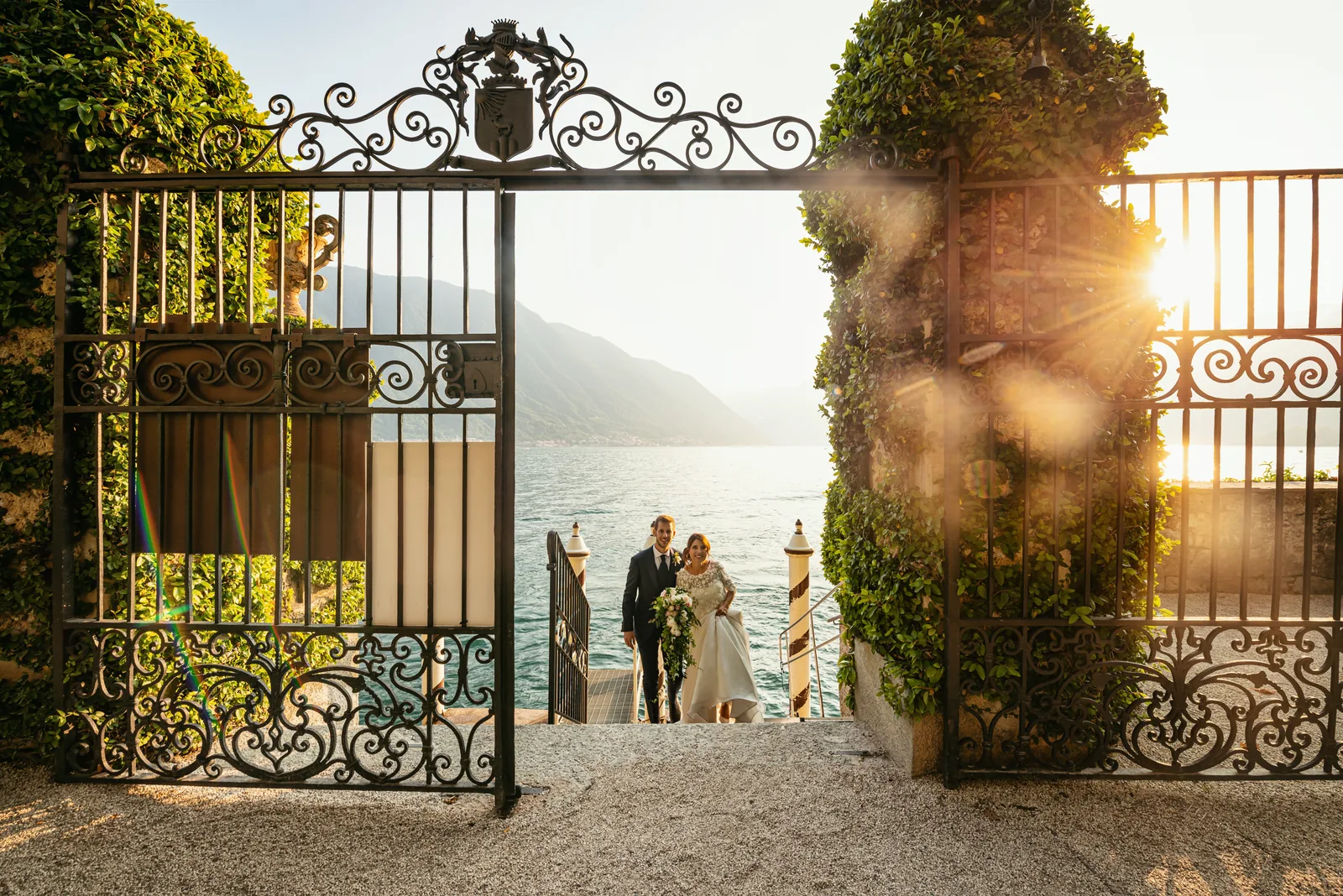The couple climbing from the lake through the iron gate of Villa del Balbianello at sunset