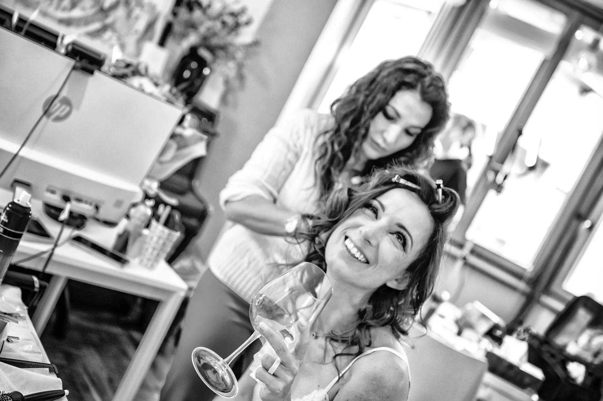 Sposa sorride durante l'acconciatura con un calice di brindisi, preparativi matrimonio Torino