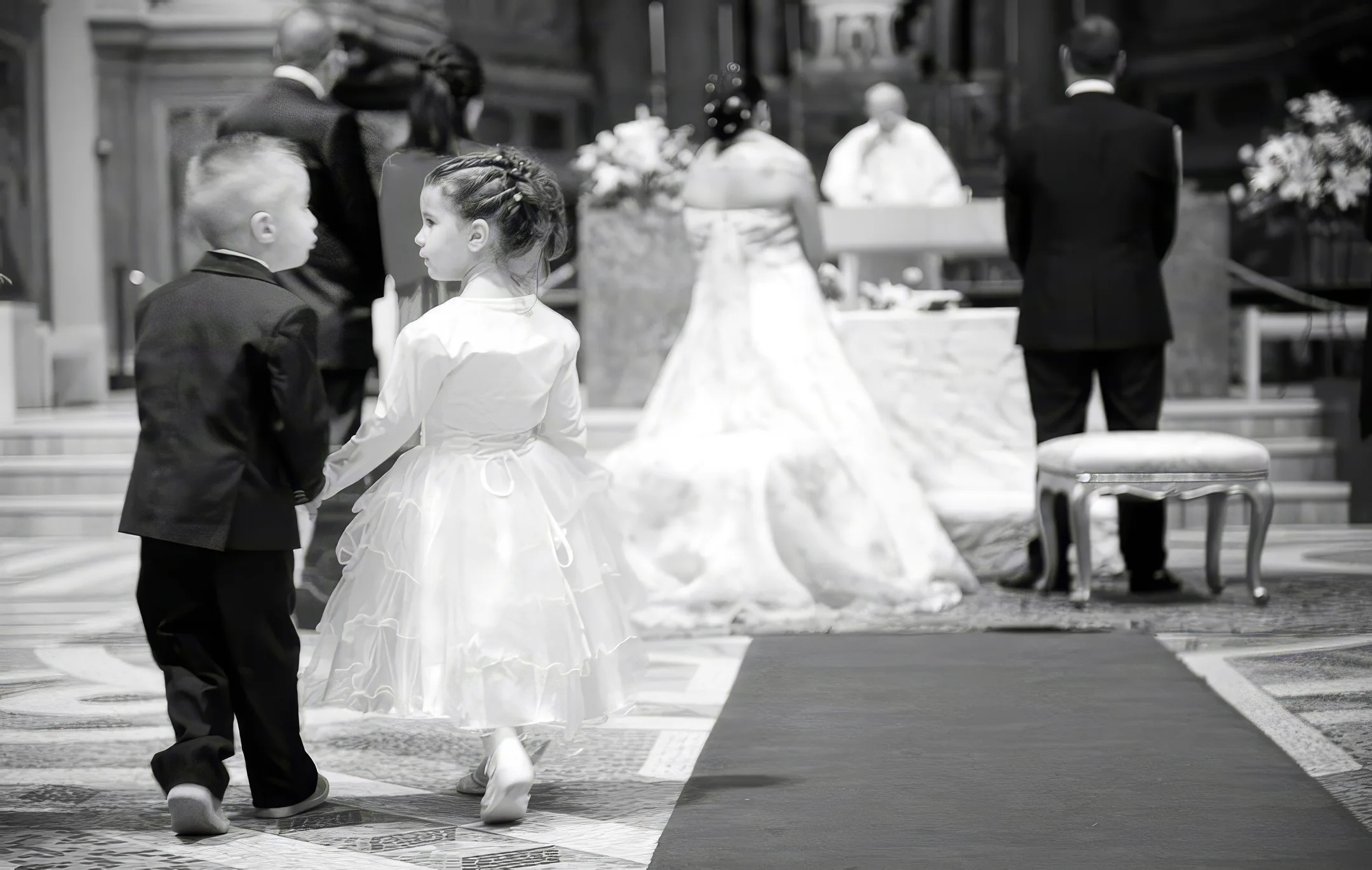 Paggetto e damigella mano nella mano lungo la navata durante la cerimonia, fotografia di reportage premiata, bianco e nero